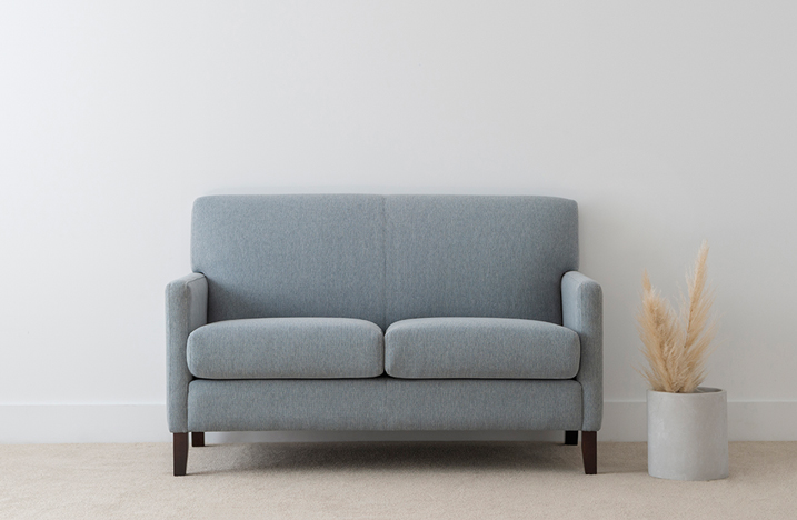 compact blue fabric sofa with narrow arms and single panel back with black timber legs